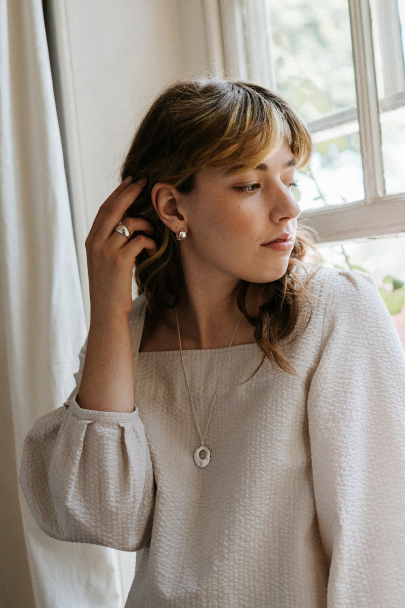 Woman in a white blouse standing by a window with white curtains
