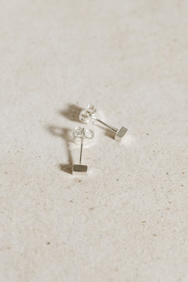 A pair of recycled sterling silver block stud earrings on a textured background.