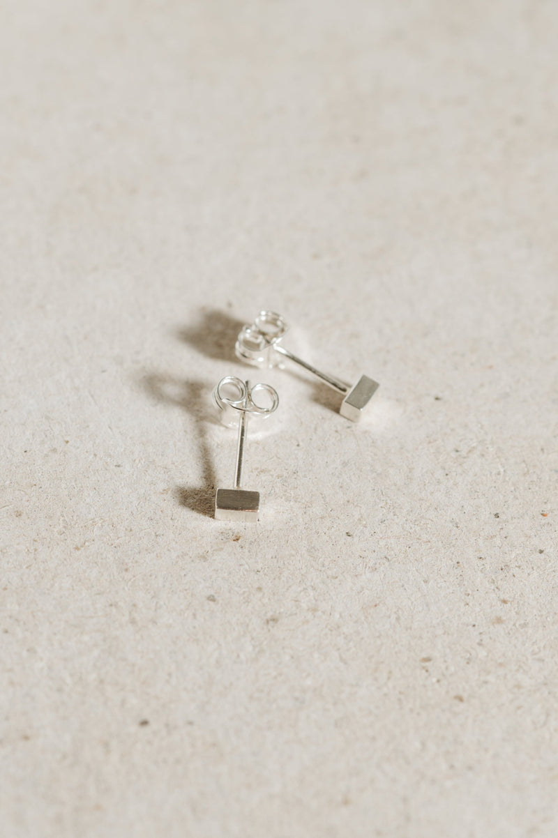 A pair of recycled sterling silver block stud earrings on a textured background.