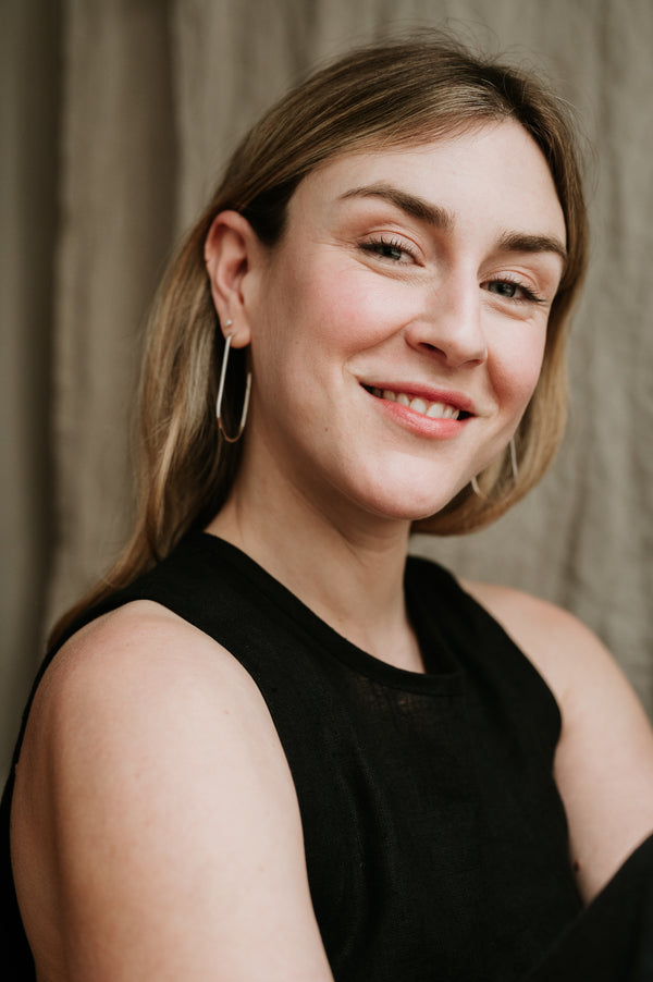 A person wearing black clothing and large hoop earrings, smiling at the camera.