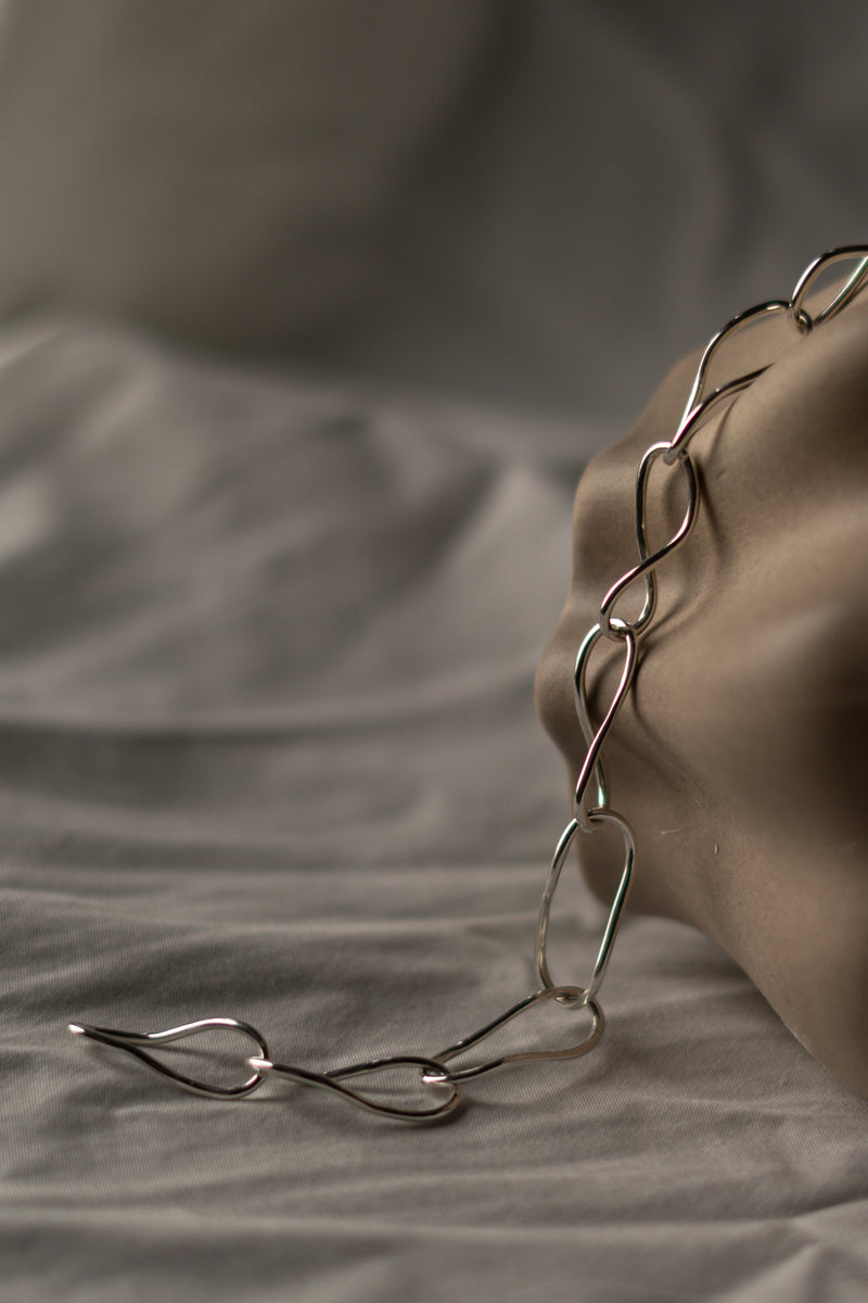 handmade eco silver link necklace laying over a vase with on a grey background