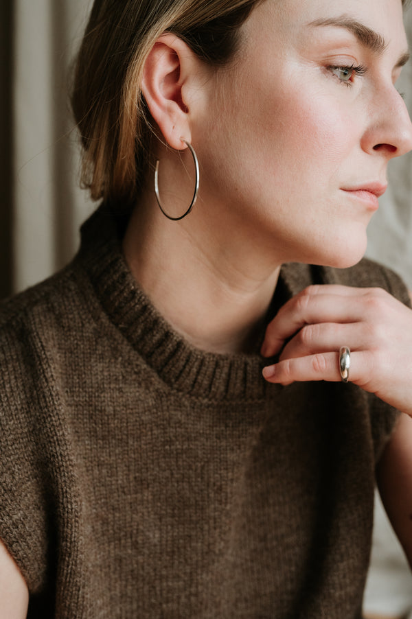 A person wearing a brown knitted sweater and large silver hoop earrings.