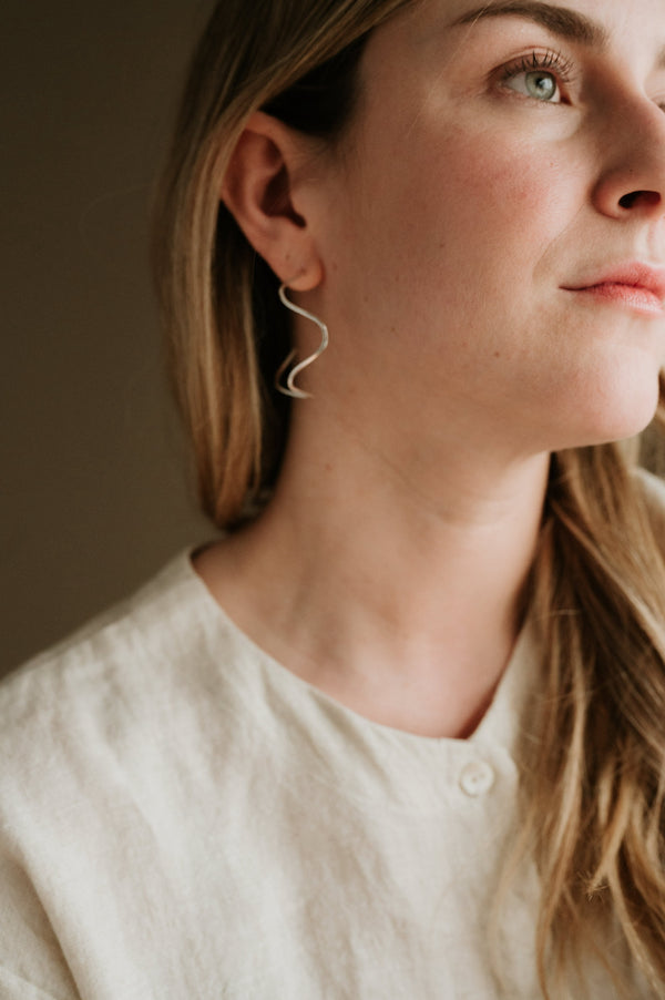 A person wearing a silver hoop earring with a textured background.