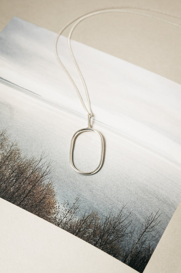 Silver necklace with an oval pendant on a snowy landscape background