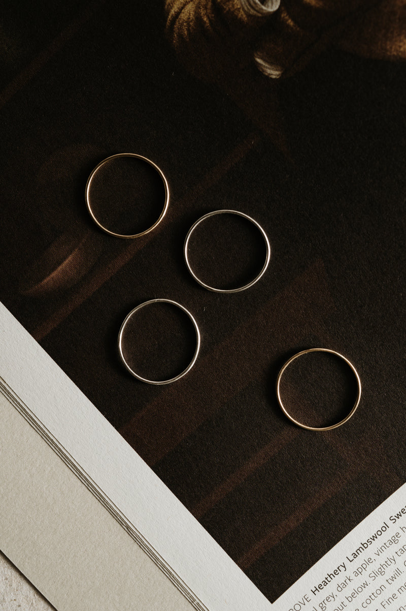 Three 9ct gold skinny stacking rings placed on a flat surface with a blurred background.