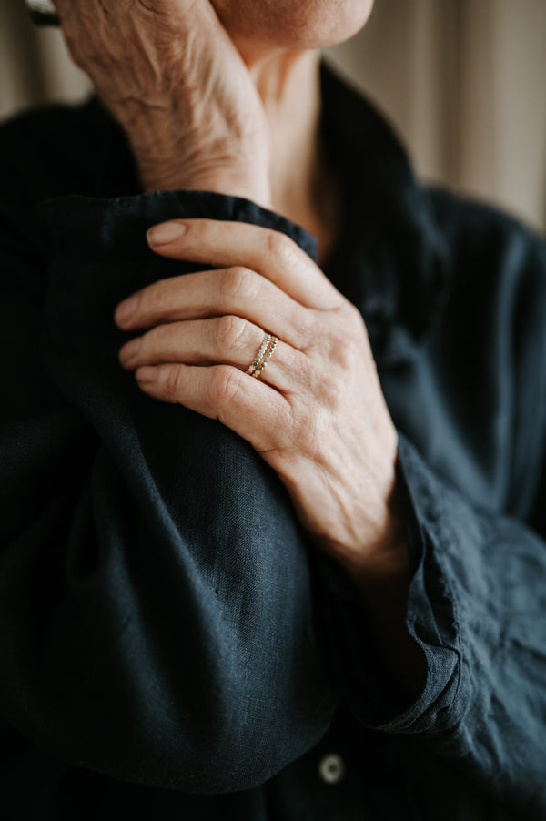 An elderly person's hand with a stack of beaded wire rings on their finger, wearing a dark outfit.