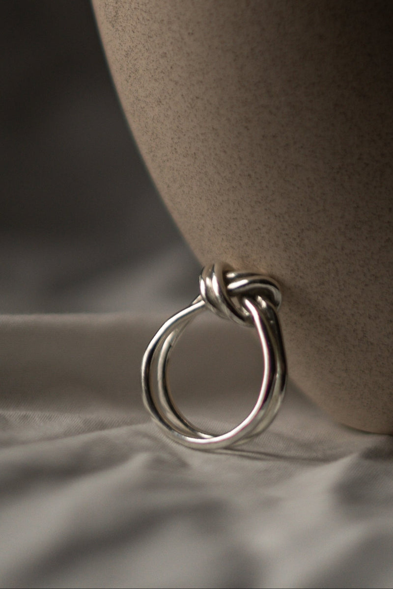 Silver knot ring on a beige ceramic vase against a neutral background