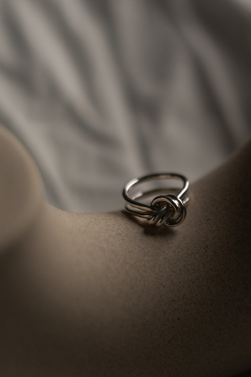 handmade silver knot ring leaning against a ceramic vase