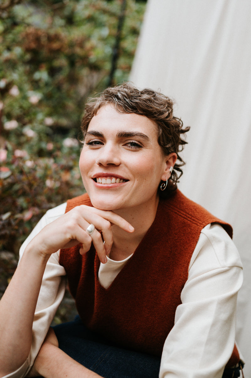 woman wearing silver sprial hoop earrings and rust wool vest