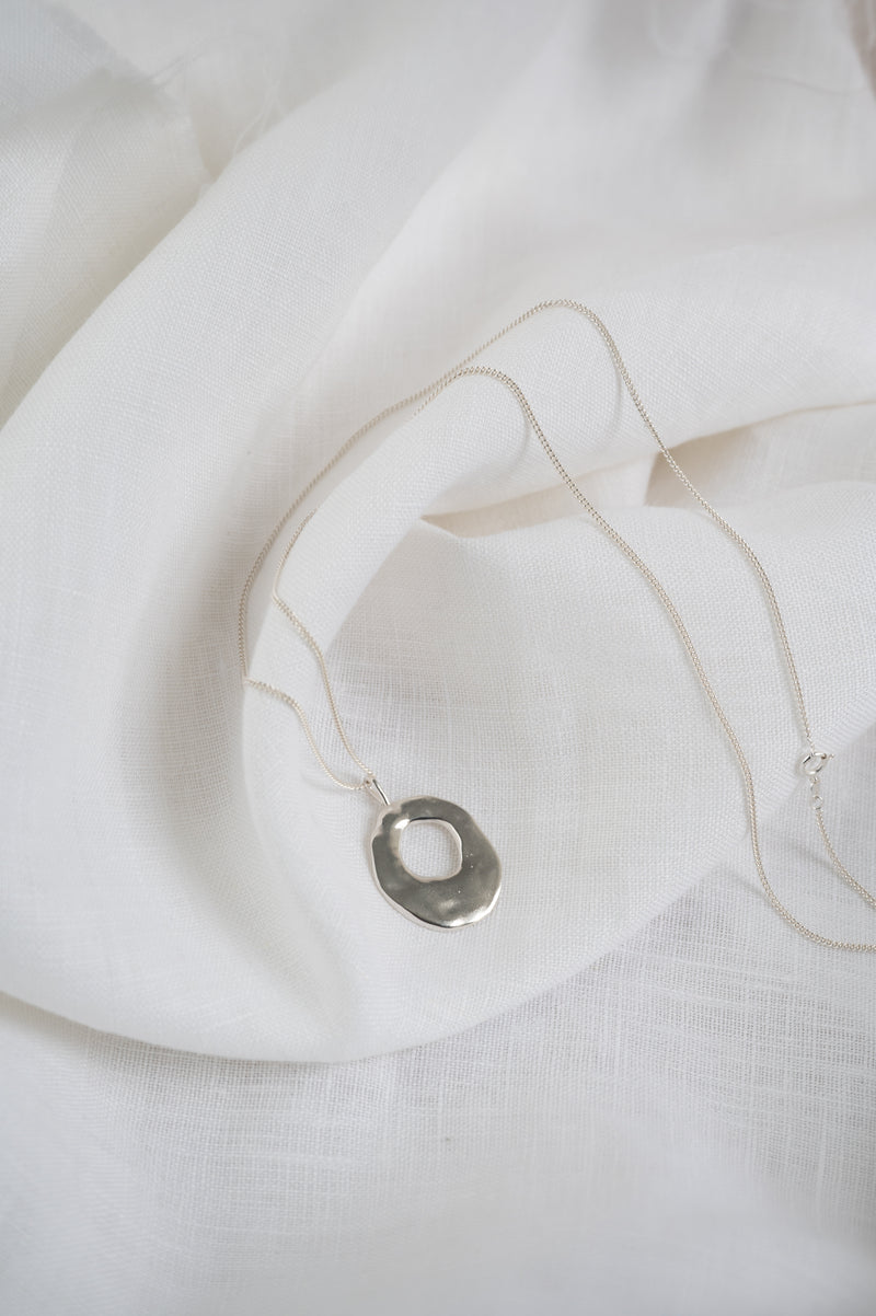 Silver necklace with a pendant on a white fabric background