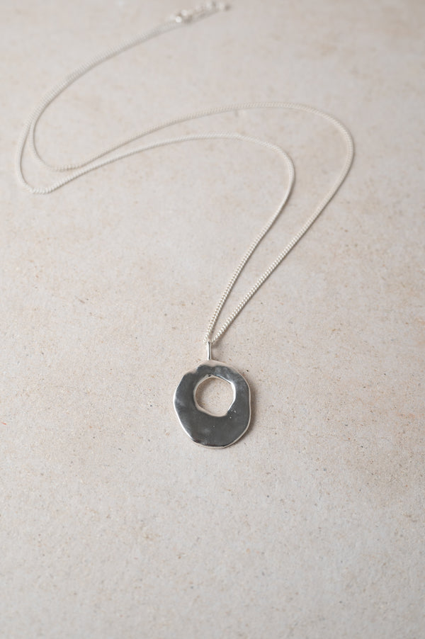 Silver necklace with a round hag stone pendant on a light background