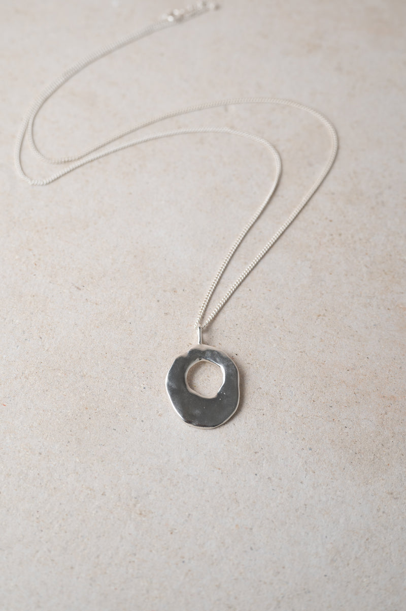 Silver necklace with a round hag stone pendant on a light background