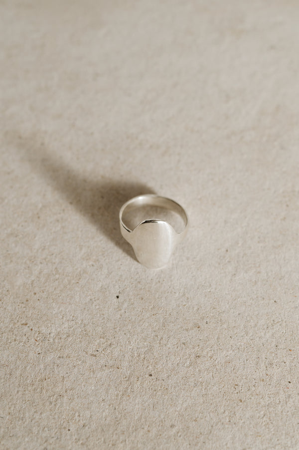 A silver oval shield ring with a smooth, shiny finish displayed on a neutral background.