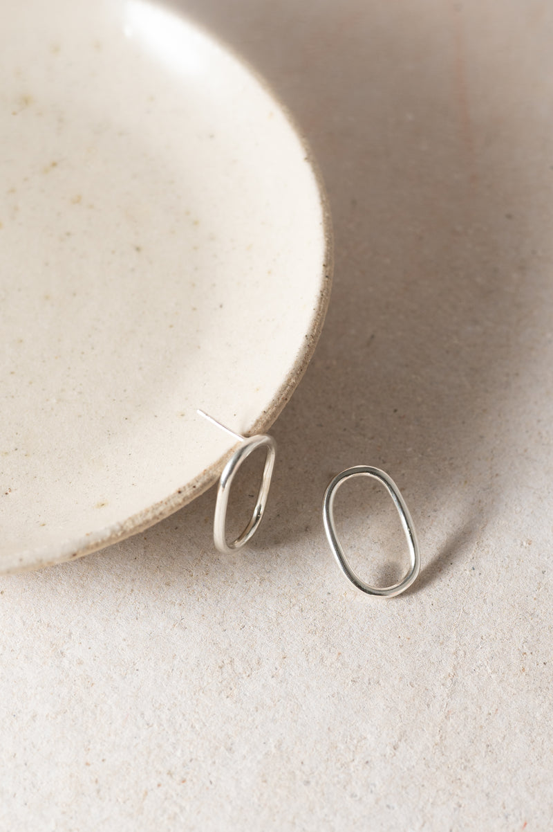 Silver oval studs earrings on a textured beige surface