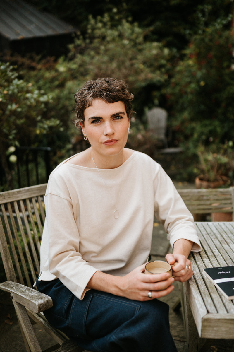 Woman sitting outdoors holding a cup, surrounded by greenery