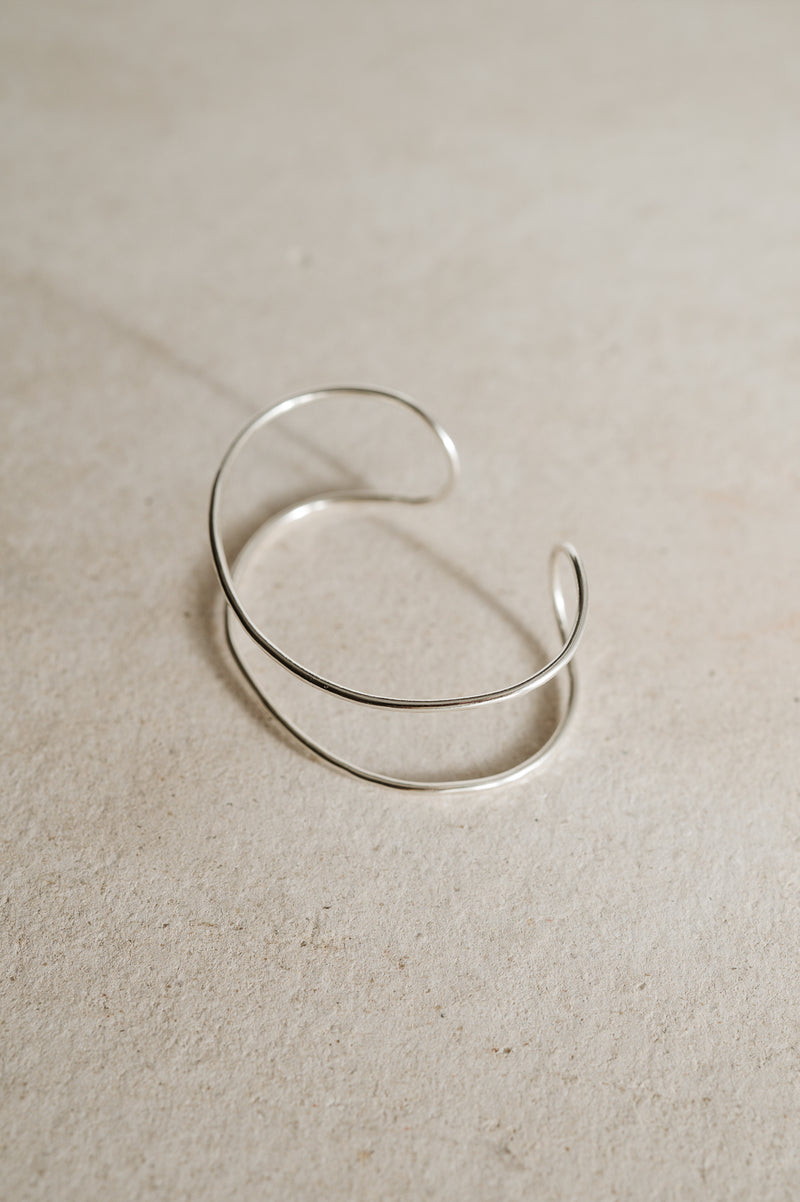 Double band silver cuff bracelet handmade from recycled Sterling Silver with open gap on a beige background