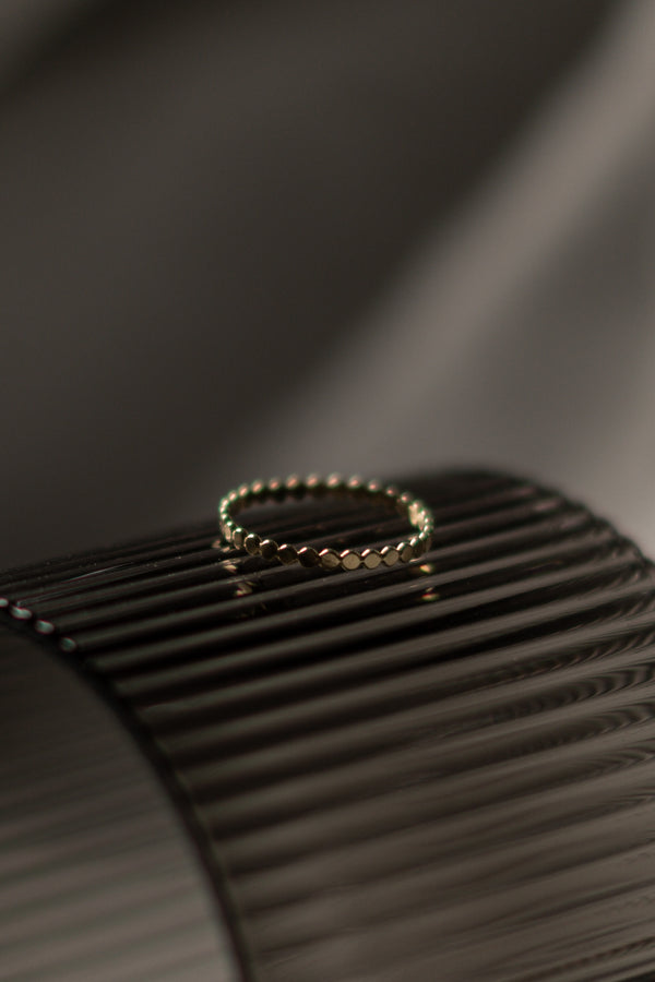 A close-up image of a gold stacking ring with beaded detailing, placed on a textured surface.