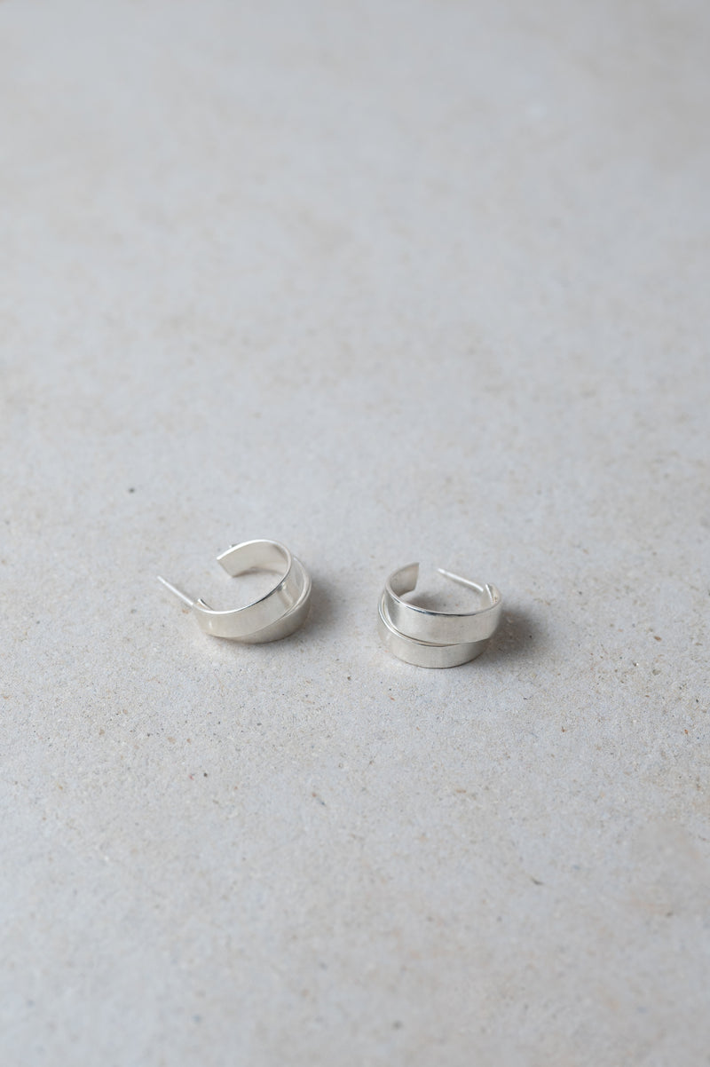 Pair of minimal handmade silver hoop earrings on a light grey background