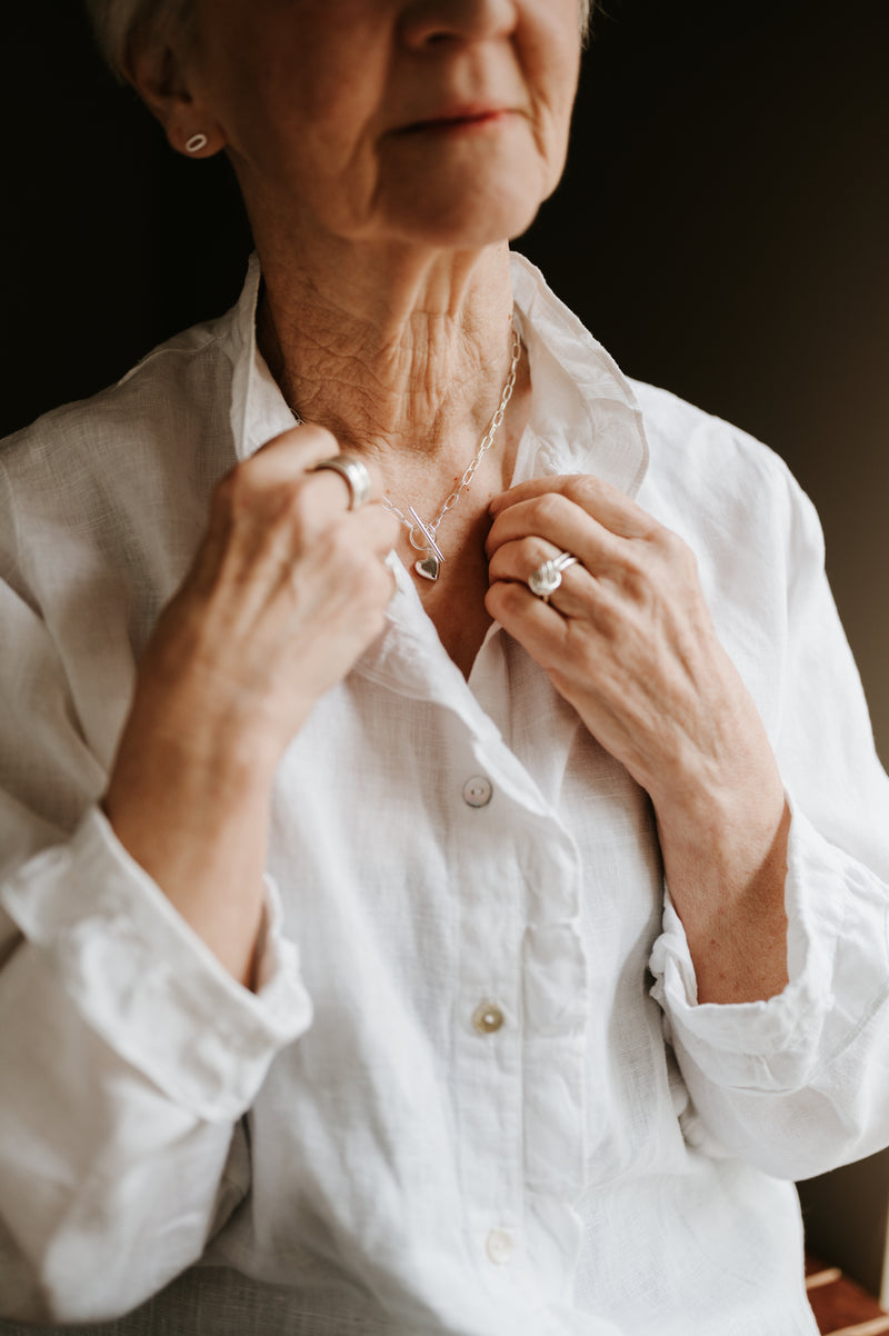 lady wearing white shirt and studio adorn necklace and rings against a dark background