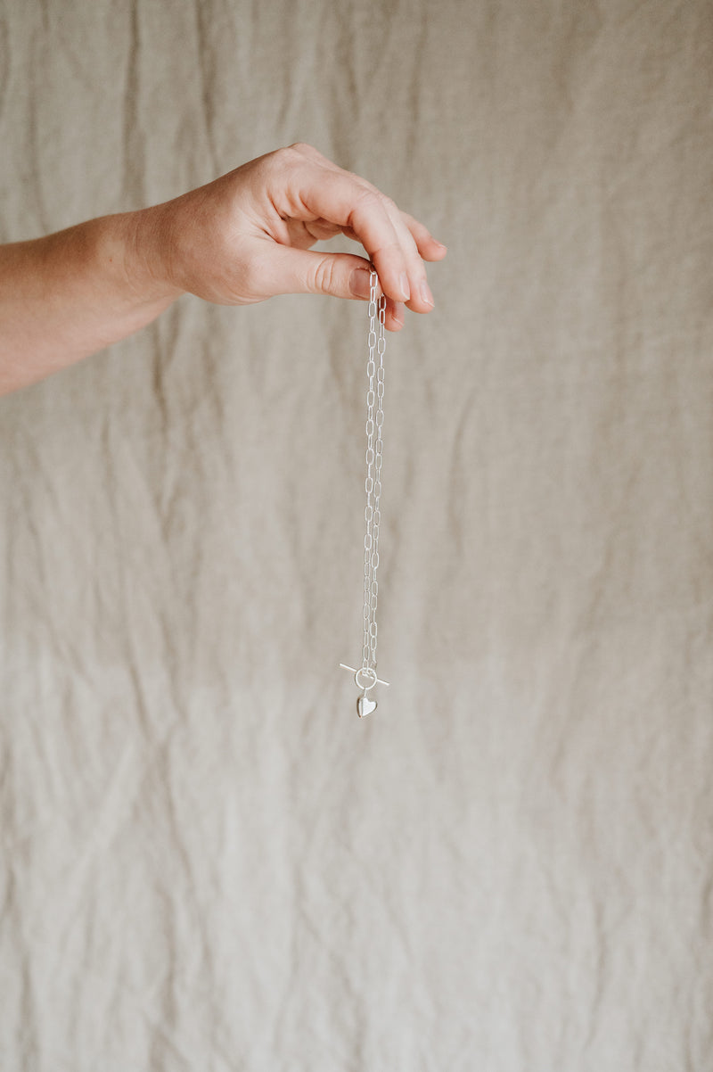 hand holding a studio adorn necklace against a beige fabric background