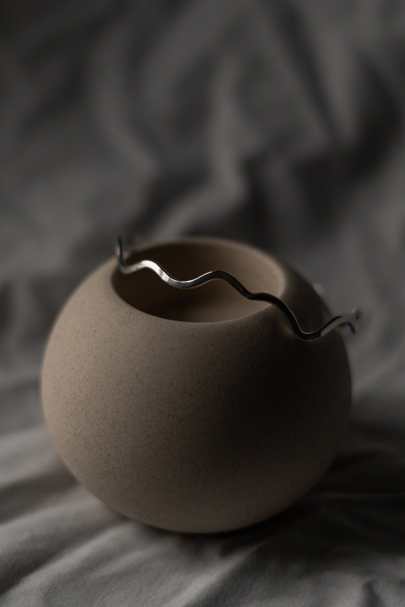 Recycled Sterling Silver Wiggle Bangle balanced on a round vase with a grey background