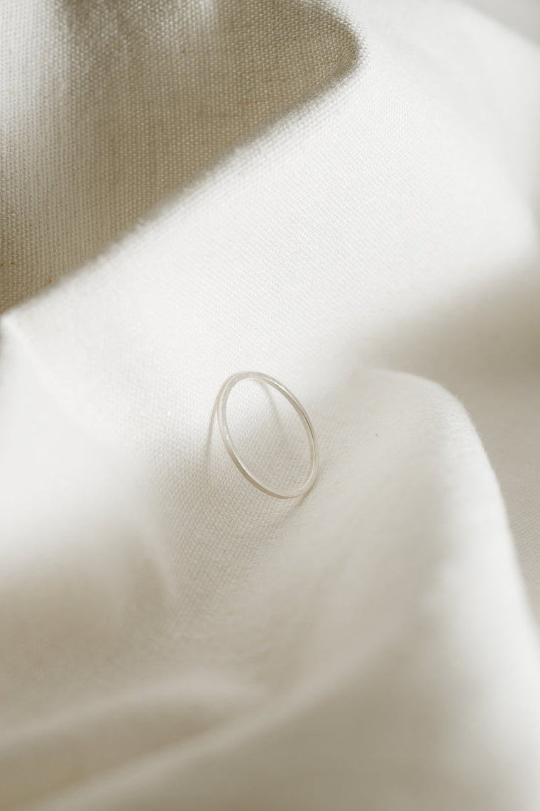 A close-up image of a silver wire stacking ring on a textured white surface.