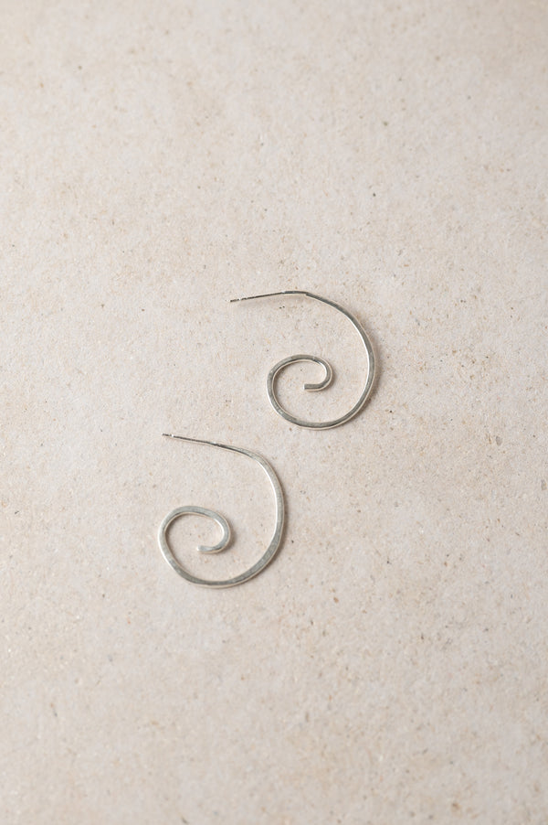 pair of handmade silver spiral earrings on a beige background