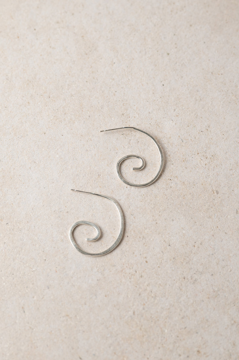 pair of handmade silver spiral earrings on a beige background