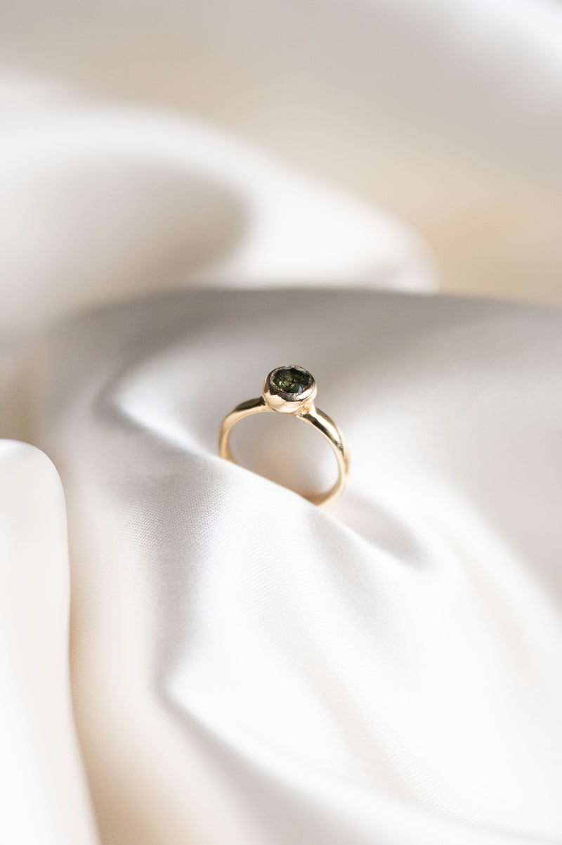 Gold ring with a green sapphire gemstone on a white fabric background