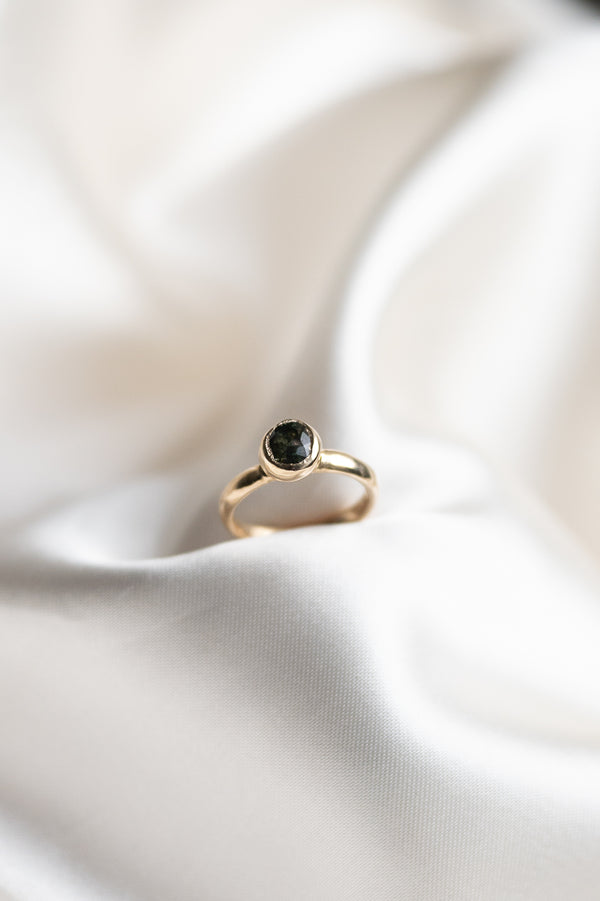 Gold ring with a green sapphire gemstone on a white satin background