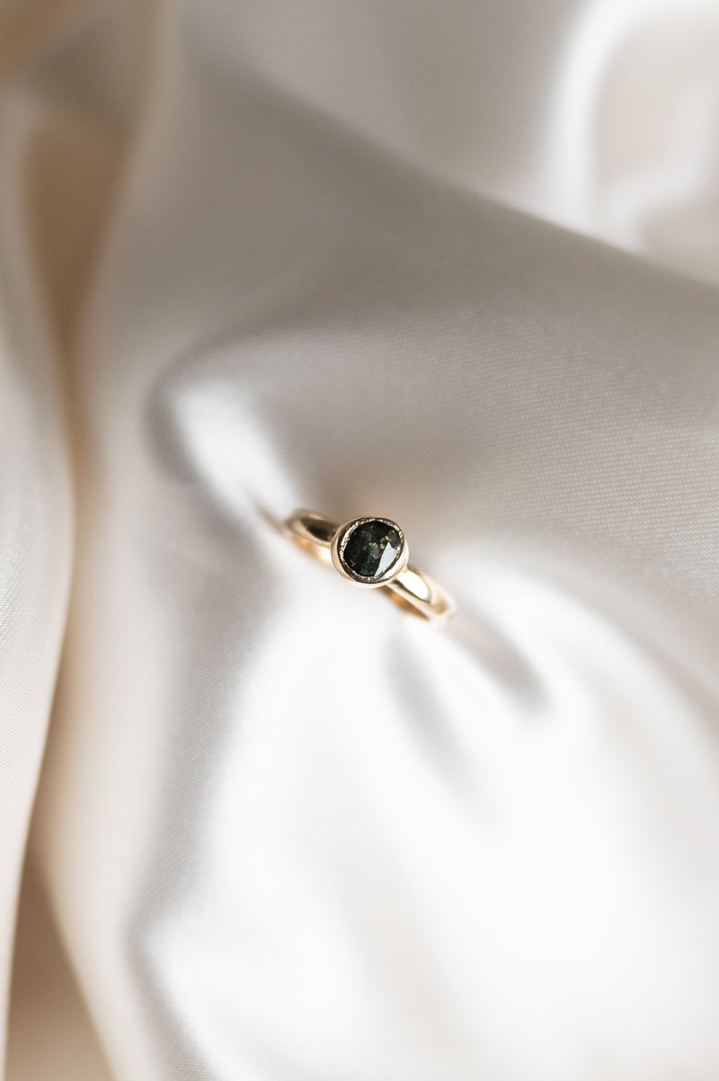 Gold ring with a green sapphire gemstone on a soft beige fabric background