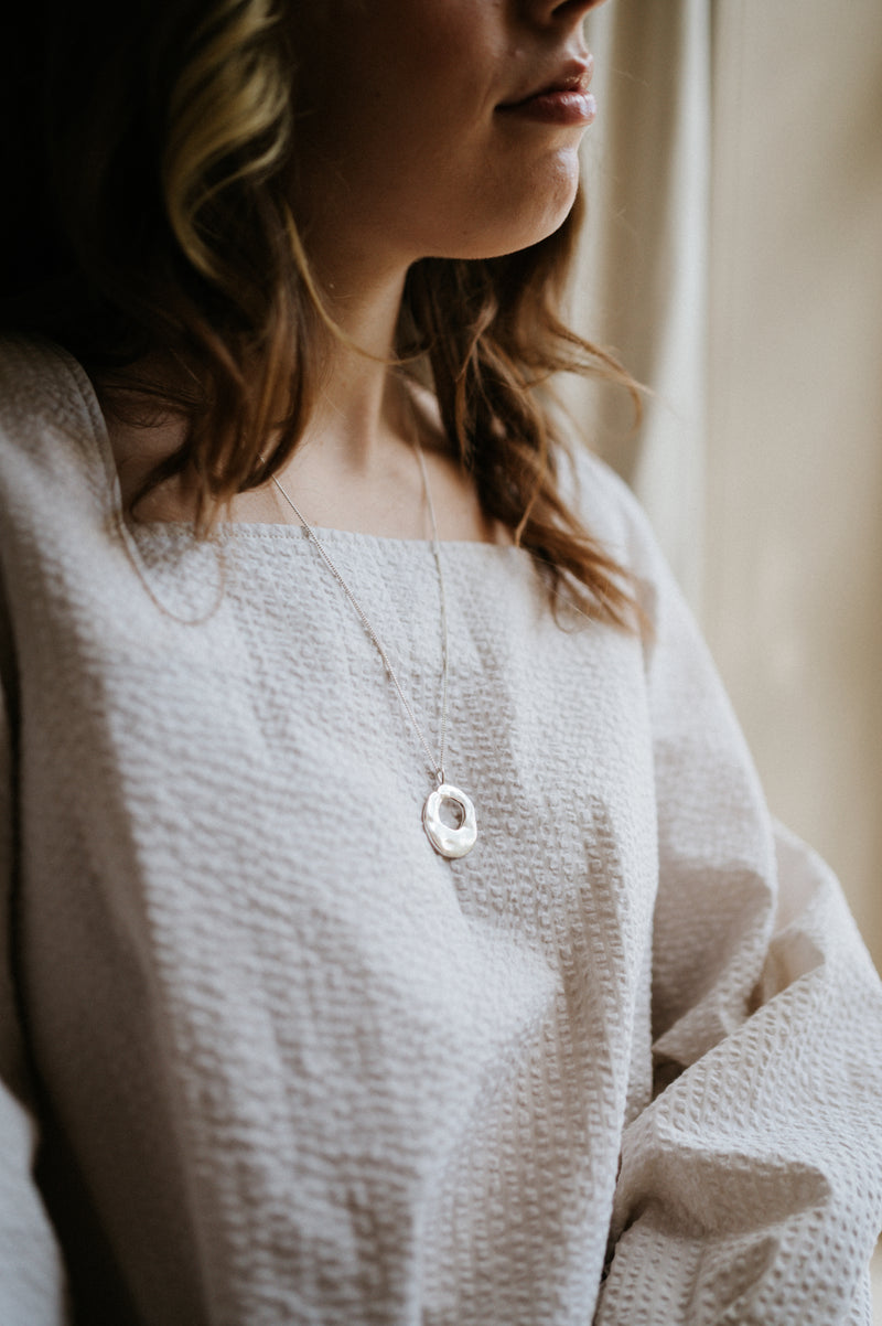 Person wearing a light-colored top with a necklace, sitting indoors.