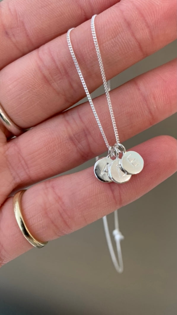 Studio Adorn model holding sterling eco silver zero waste pebble necklace with additional silver pebbles stamped with uppercase initials