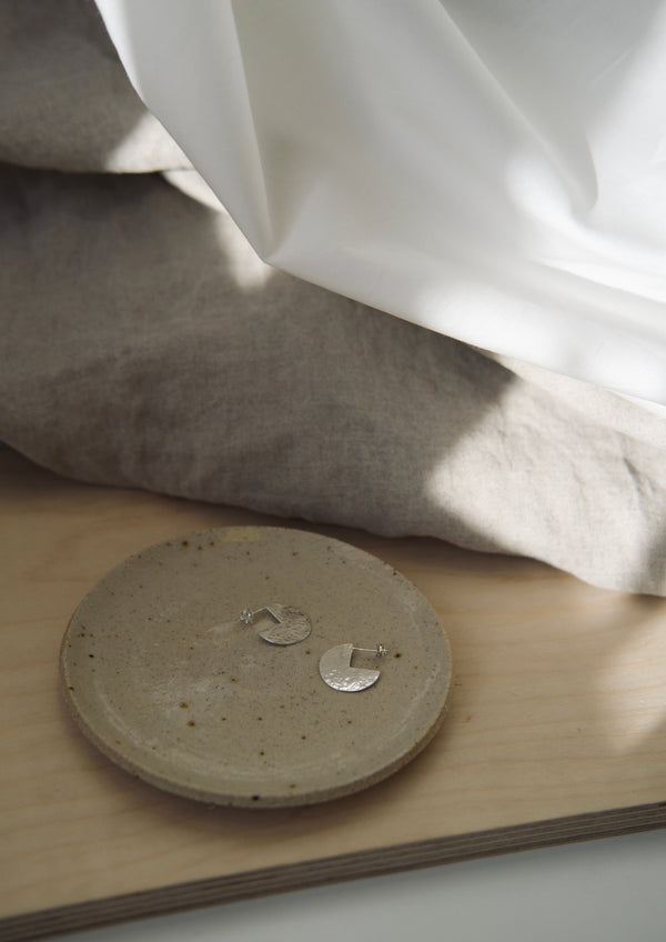 A beige ceramic trinket dish on a wooden surface with a piece of white cloth in the background.