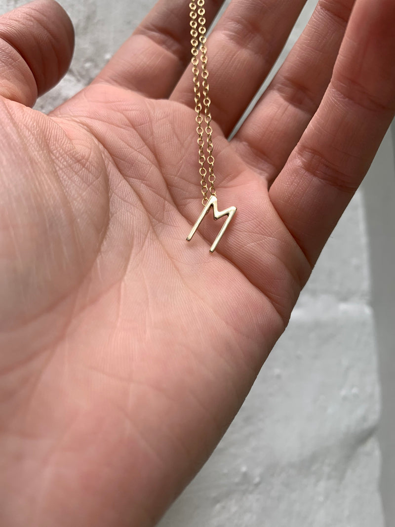 Studio Adorn zoomed in image of model holding 9ct mini initial pendant necklace with gold fine trace chain 