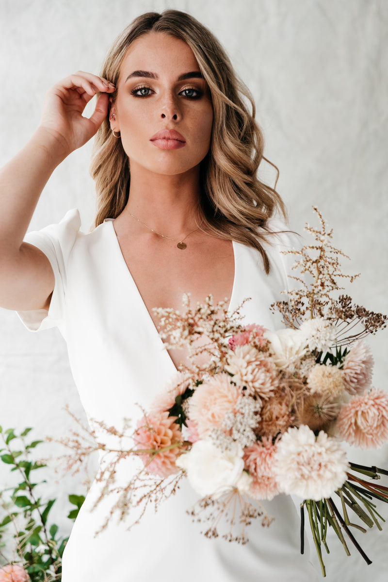 Studio Adorn front profile of model wearing gold hammered disc necklace holding bouquet of flowers