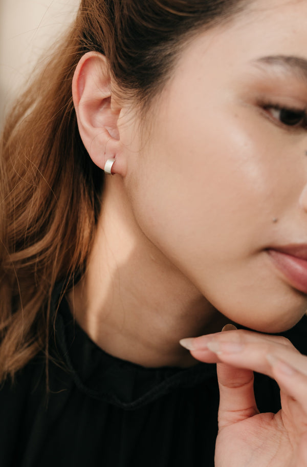 A close-up image of a person wearing small silver hoop earrings.